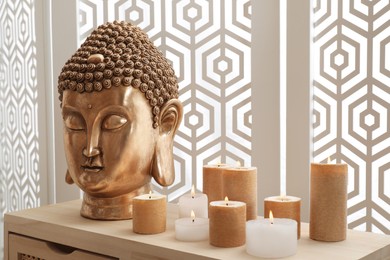 Photo of Buddha statue and burning candles on table indoors