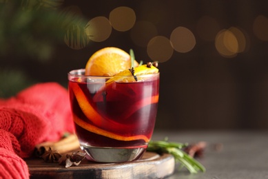 Photo of Glass with aromatic mulled wine on grey table against festive lights. Space for text