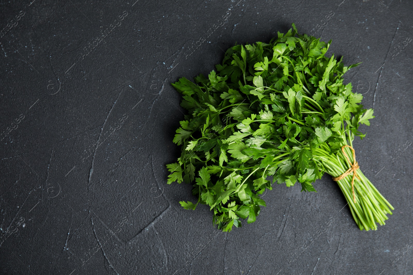 Photo of Bunch of fresh green parsley on dark background, view from above. Space for text