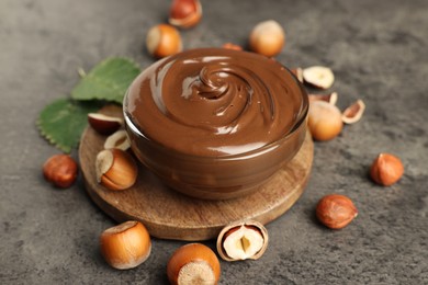 Glass bowl with tasty chocolate hazelnut spread and nuts on grey table
