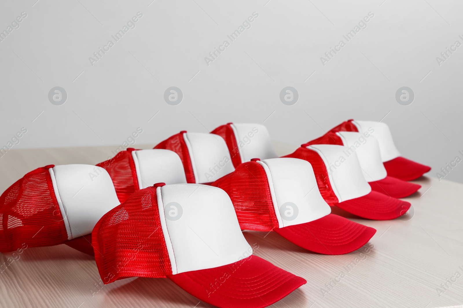 Photo of Many blank colorful caps on wooden table near light wall. Mock up for design