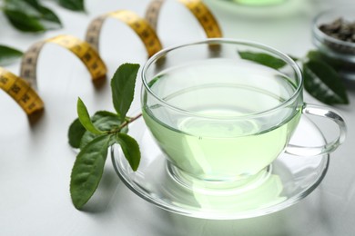 Photo of Cup of herbal diet tea and measuring tape on light table