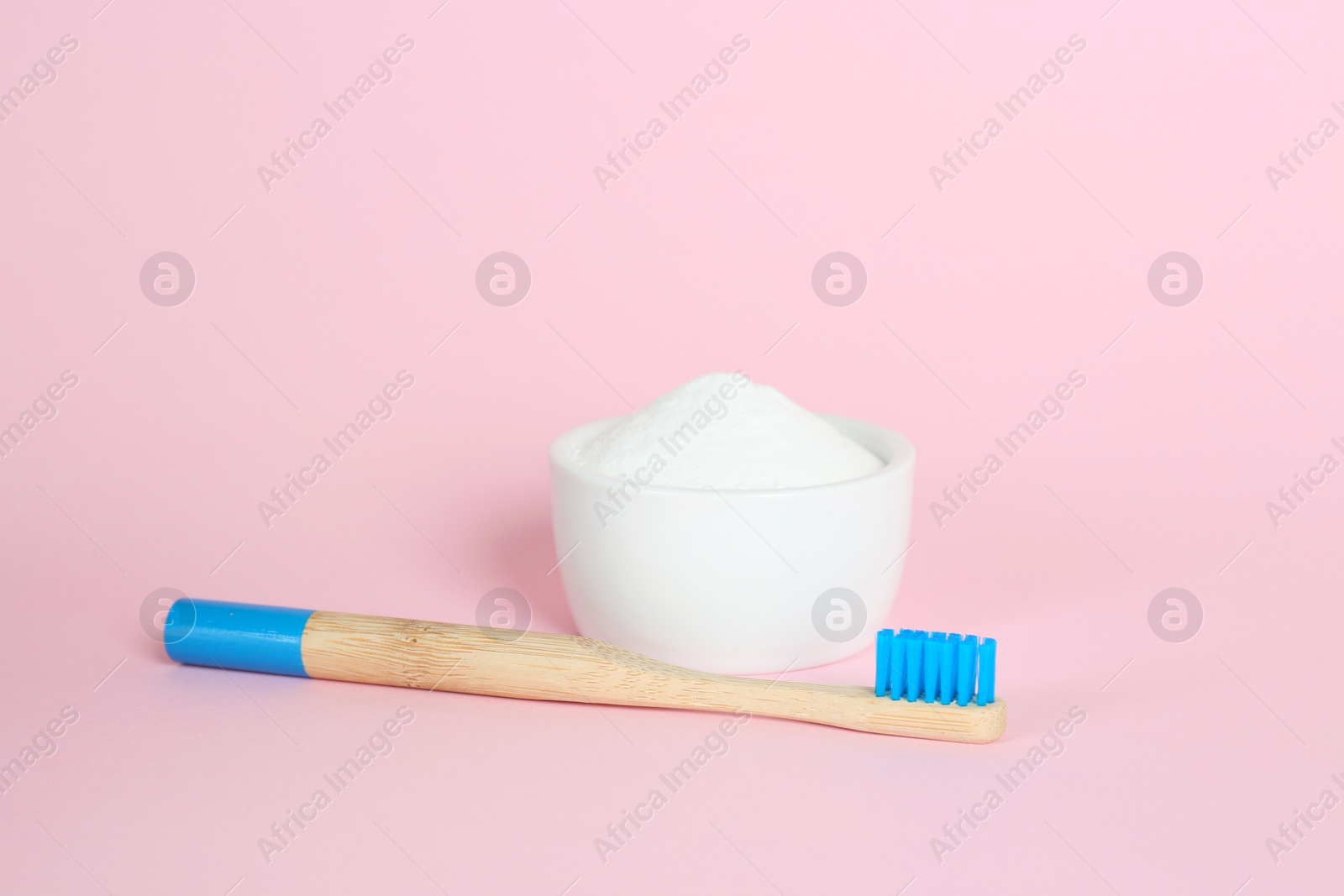 Photo of Bamboo toothbrush and bowl with baking soda on pink background