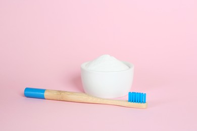 Bamboo toothbrush and bowl with baking soda on pink background
