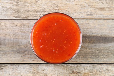 Photo of Spicy chili sauce in bowl on wooden table, top view