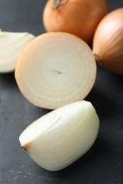 Photo of Whole and cut onions on black textured table, closeup