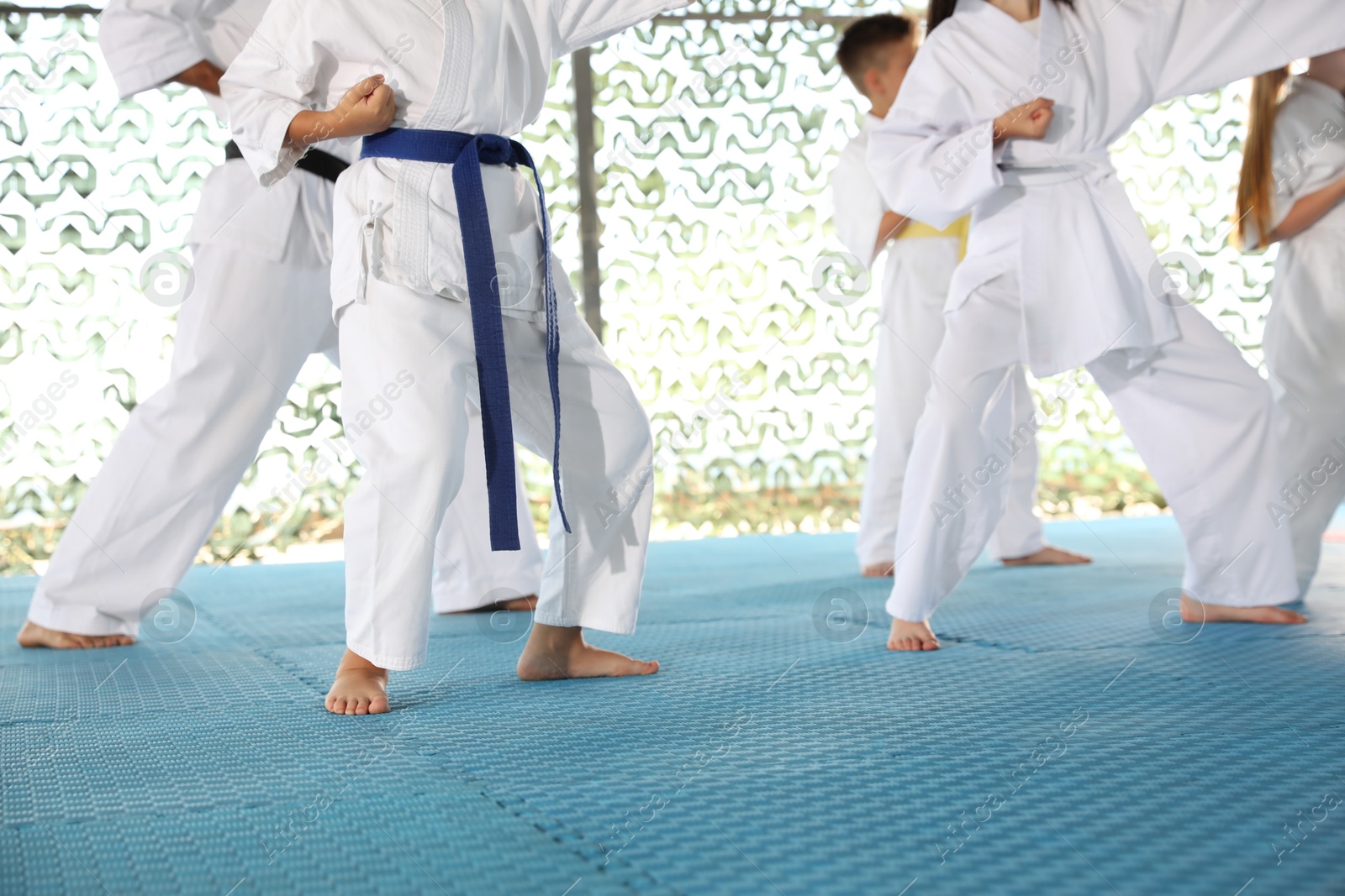 Photo of Children in kimono practicing karate on tatami outdoors, closeup