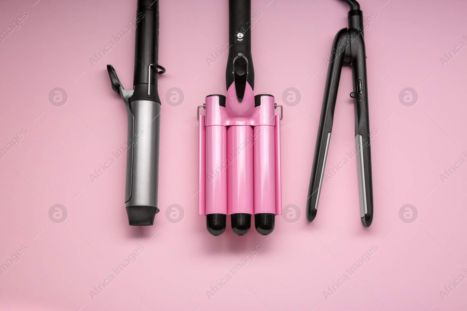 Photo of Different hair irons on pink background, flat lay
