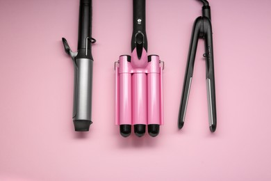 Different hair irons on pink background, flat lay