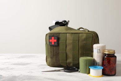 Photo of Military first aid kit, tourniquet, pills and elastic bandage on light grey table, space for text