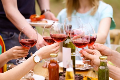 Photo of Young people with glasses wine at table outdoors. Summer barbecue