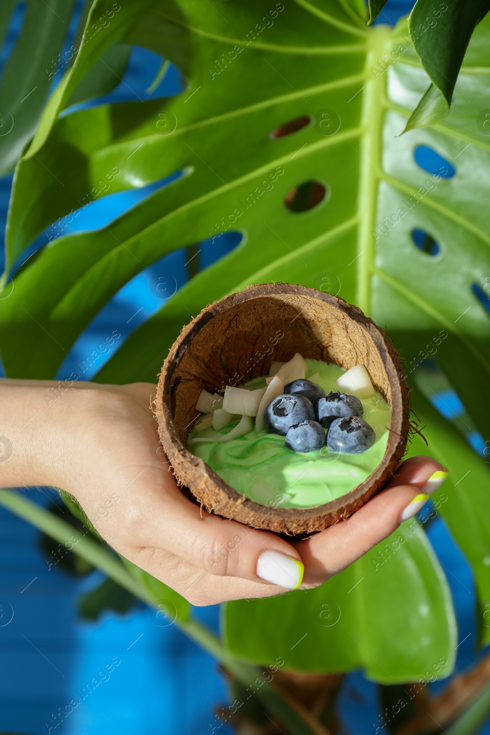 Photo of Woman holding coconut shell with tasty smoothie bowl on blurred background, closeup