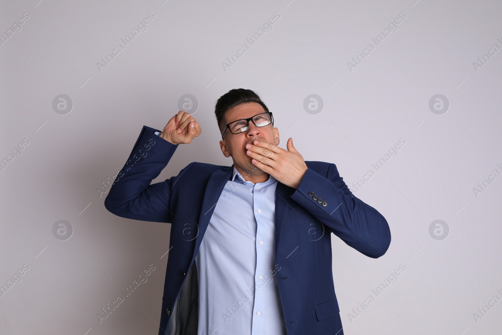 Photo of Handsome tired businessman yawning on light grey background