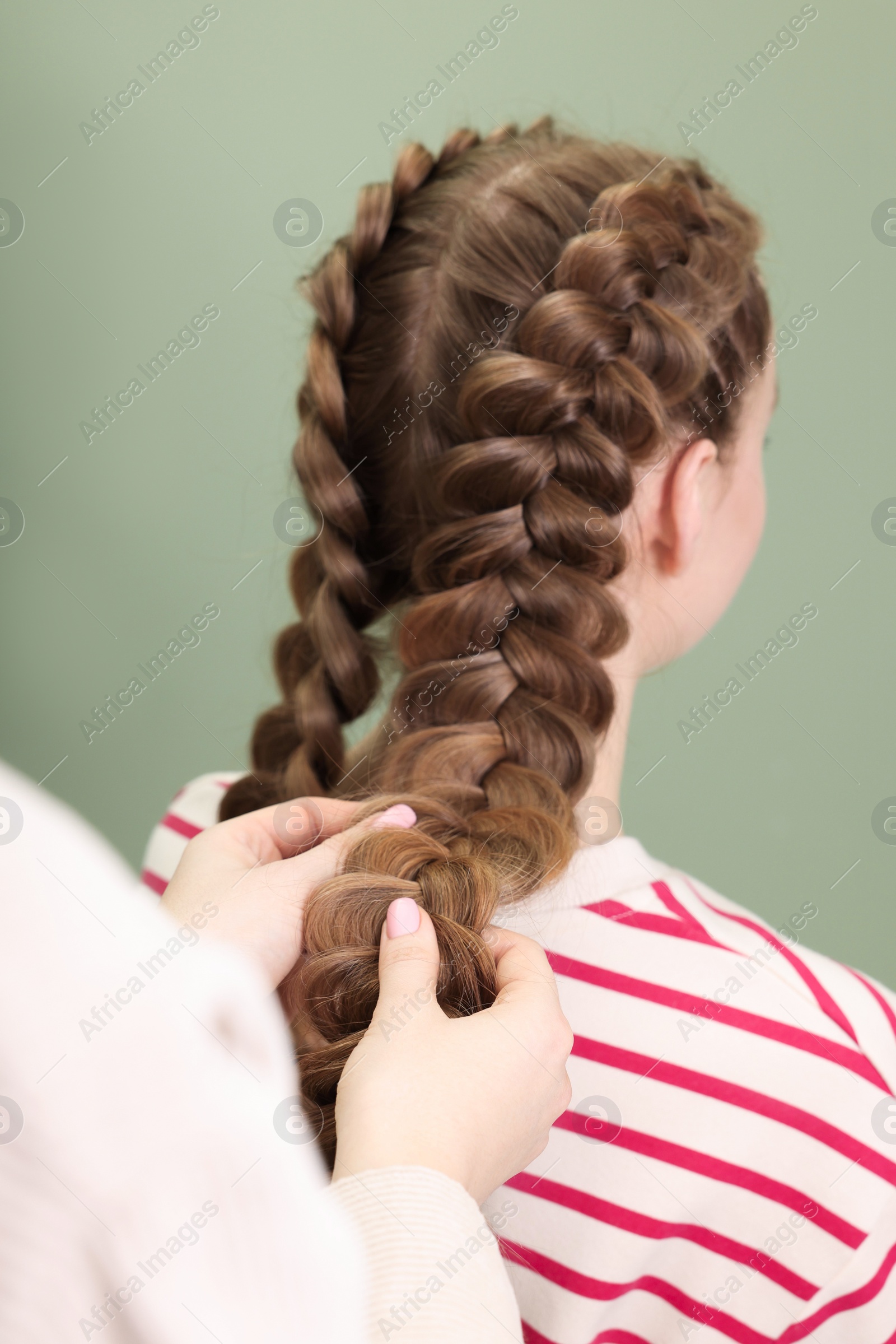 Photo of Professional stylist braiding woman's hair on olive background, closeup