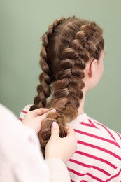 Professional stylist braiding woman's hair on olive background, closeup