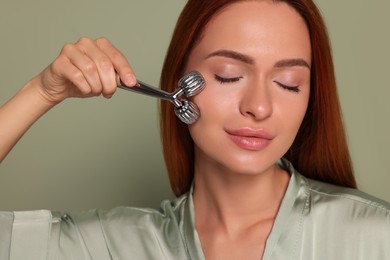 Photo of Young woman massaging her face with metal roller on green background