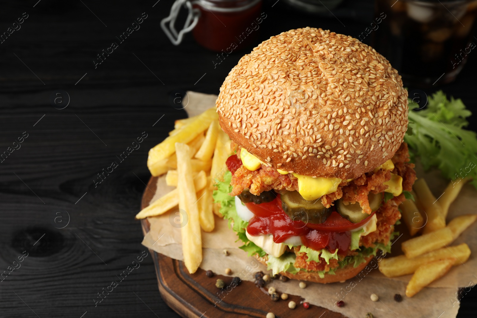 Photo of Delicious burger with crispy chicken patty and french fries on black wooden table, closeup. Space for text