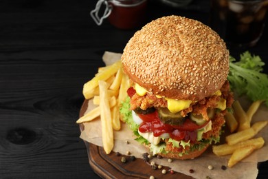 Photo of Delicious burger with crispy chicken patty and french fries on black wooden table, closeup. Space for text