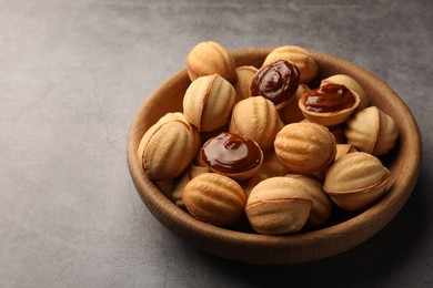 Photo of Delicious nut shaped cookies with boiled condensed milk in wooden bowl on gray textured table