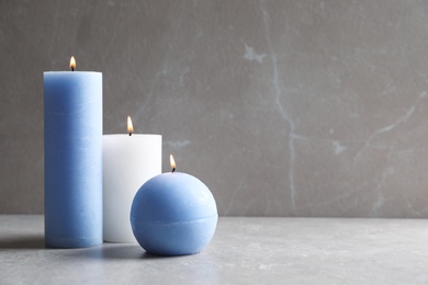 Photo of Beautiful burning wax candles on table against grey background