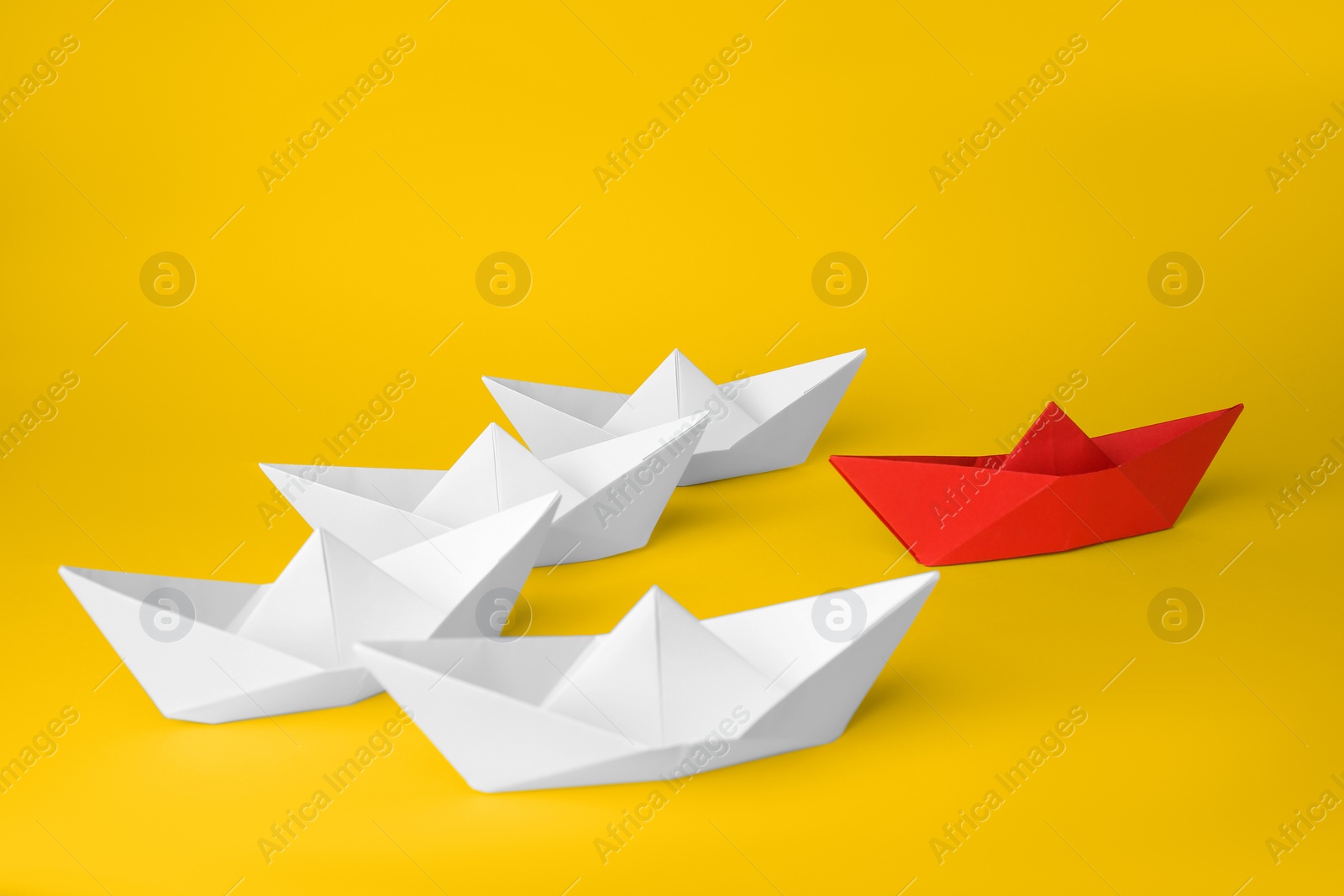 Photo of Group of paper boats following red one on yellow background. Leadership concept