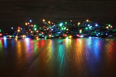 Photo of Beautiful colorful Christmas lights on wooden table. Space for text