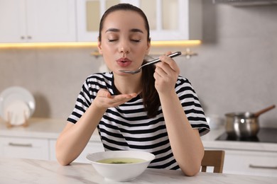 Photo of Beautiful woman eating tasty soup at white table in kitchen