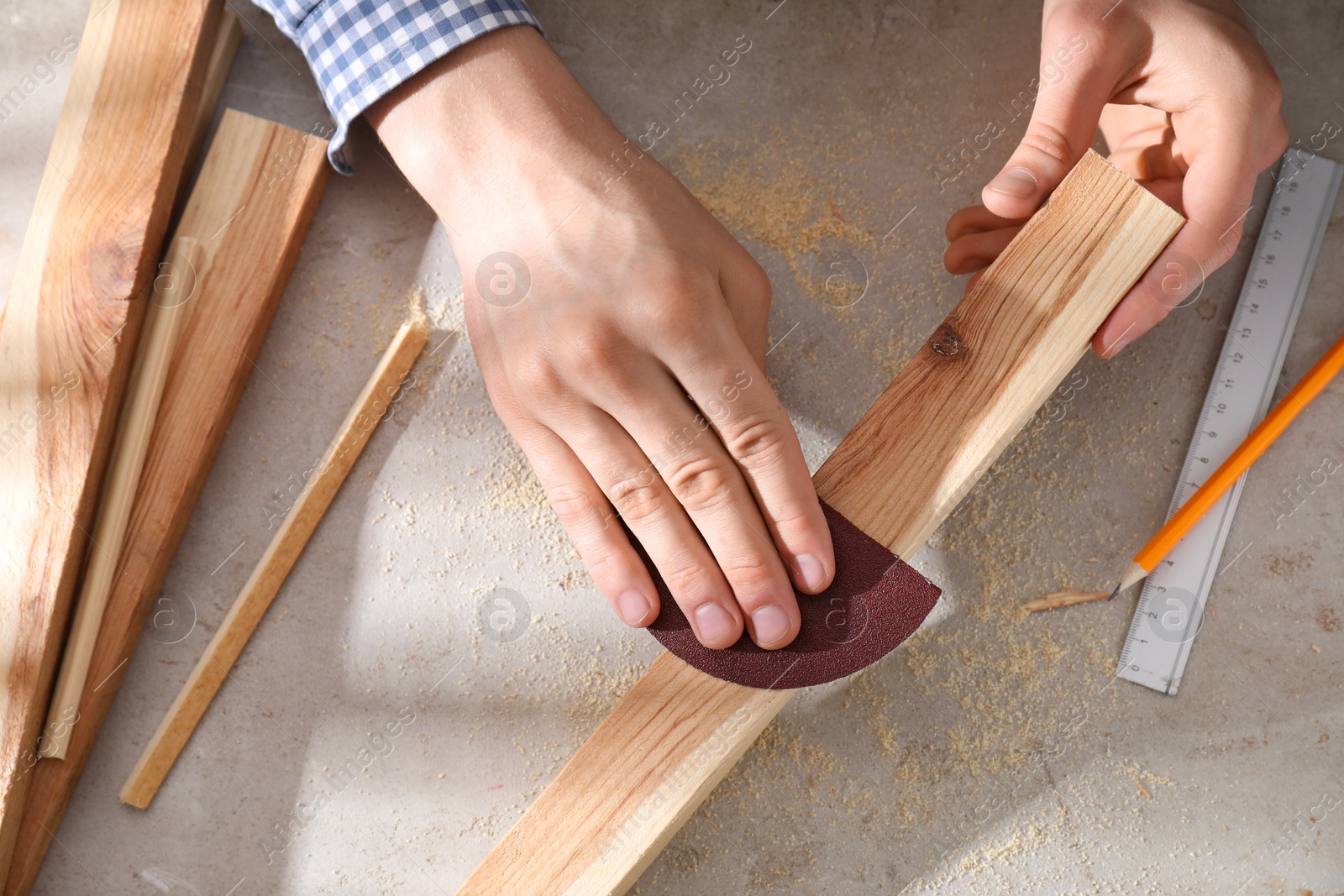 Photo of Man polishing wooden plank with sandpaper at grey table, top view