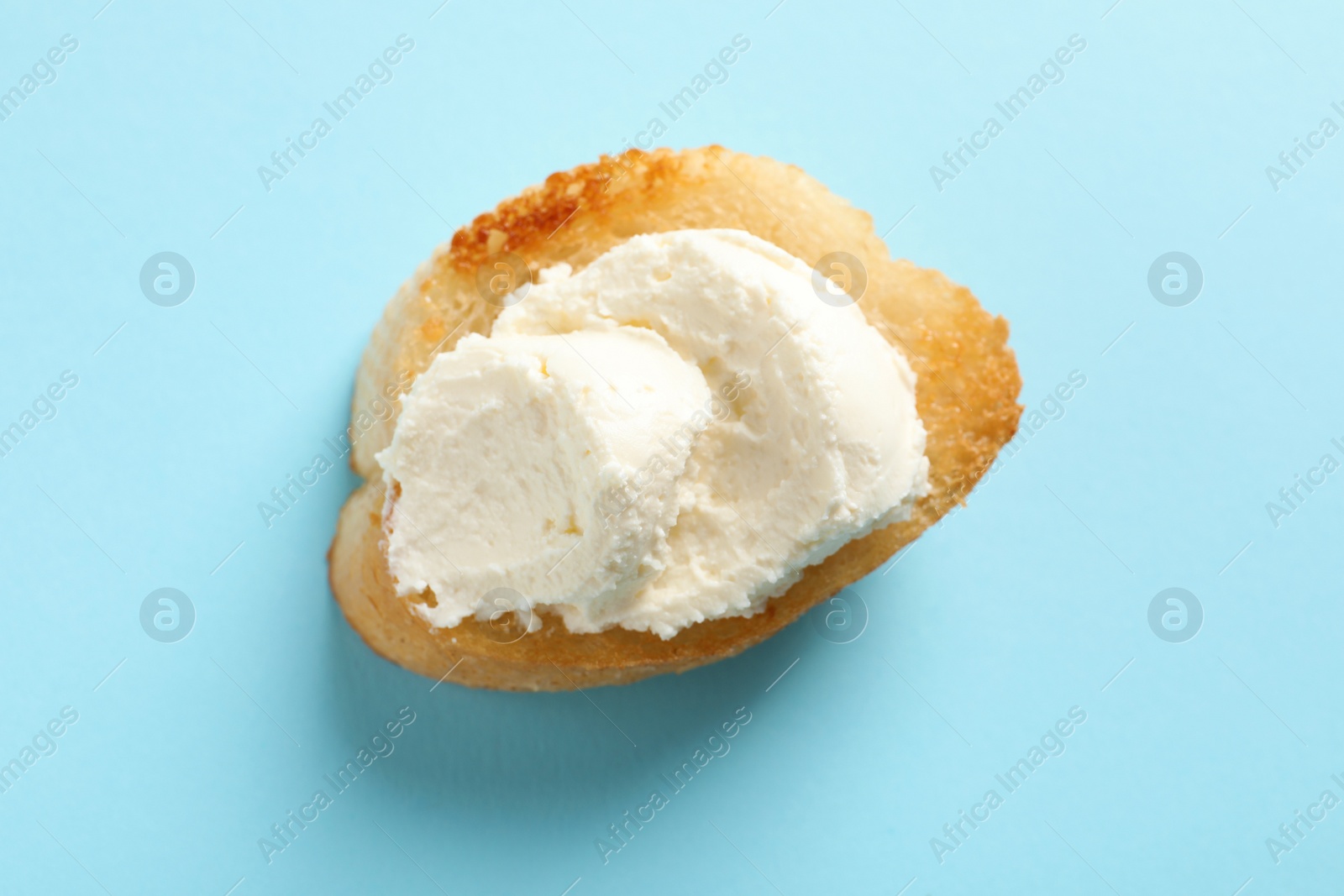 Photo of Piece of baguette with tasty cream cheese on color background, top view