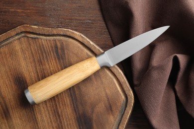 Photo of One sharp knife, cloth and board on wooden table, top view