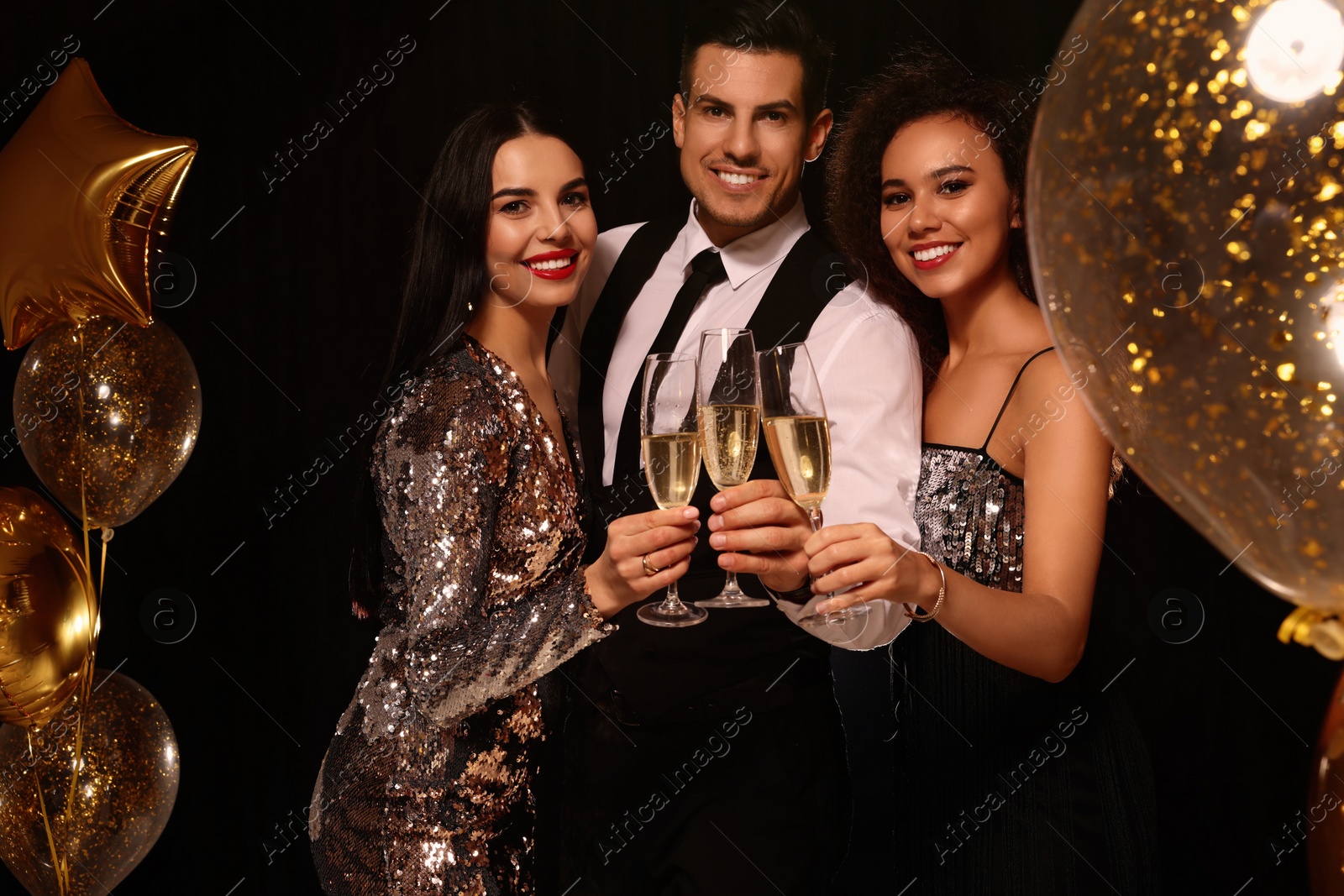 Photo of Happy friends with glasses of sparkling wine celebrating New Year on black background