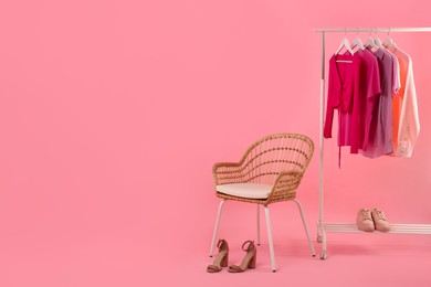 Photo of Rack with different stylish women`s clothes, shoes and armchair on pink background, space for text