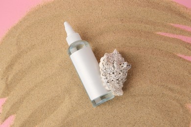 Bottle of serum and seashell on sand against pink background, top view