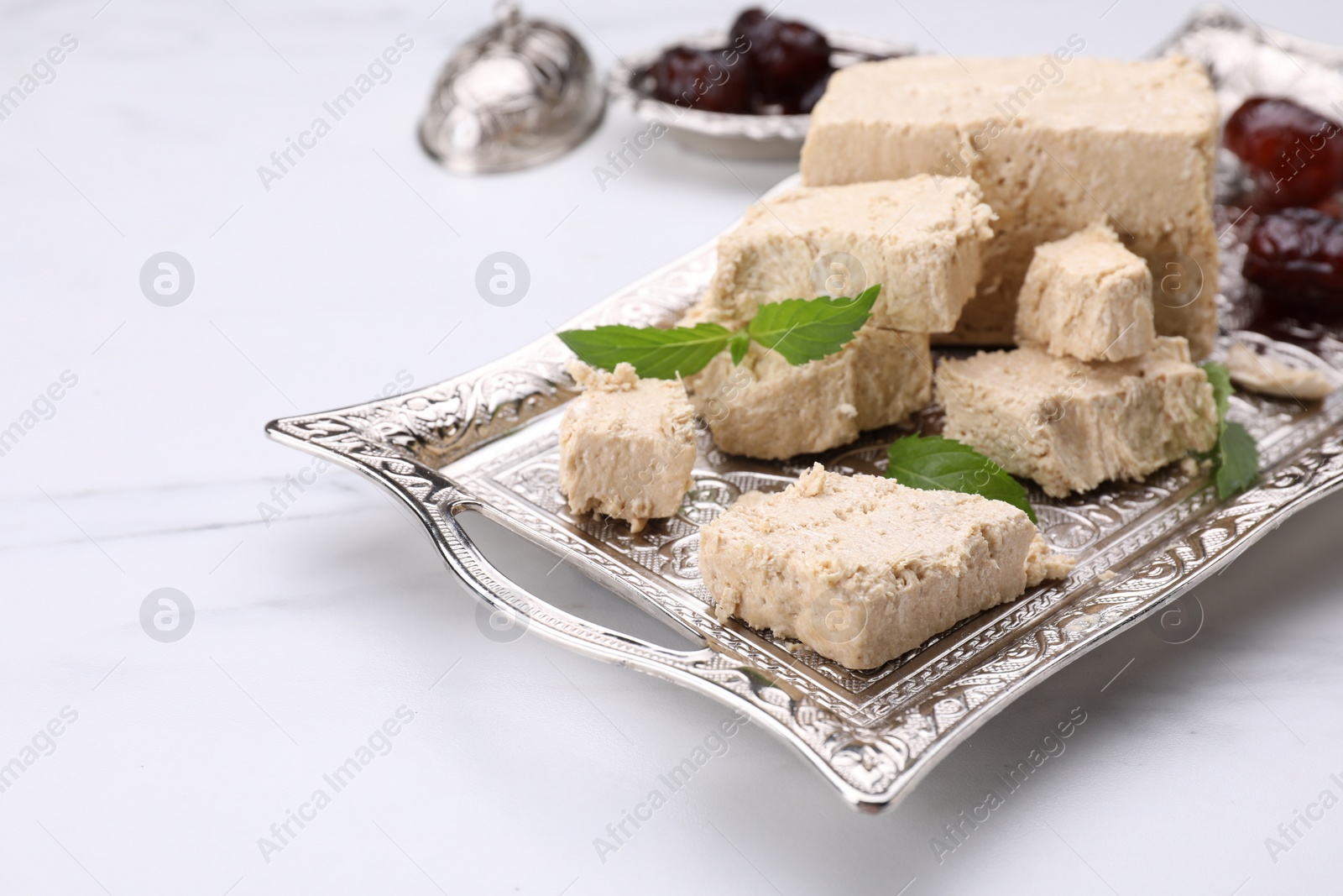 Photo of Pieces of tasty halva, dates and mint leaves on white marble table, closeup. Space for text