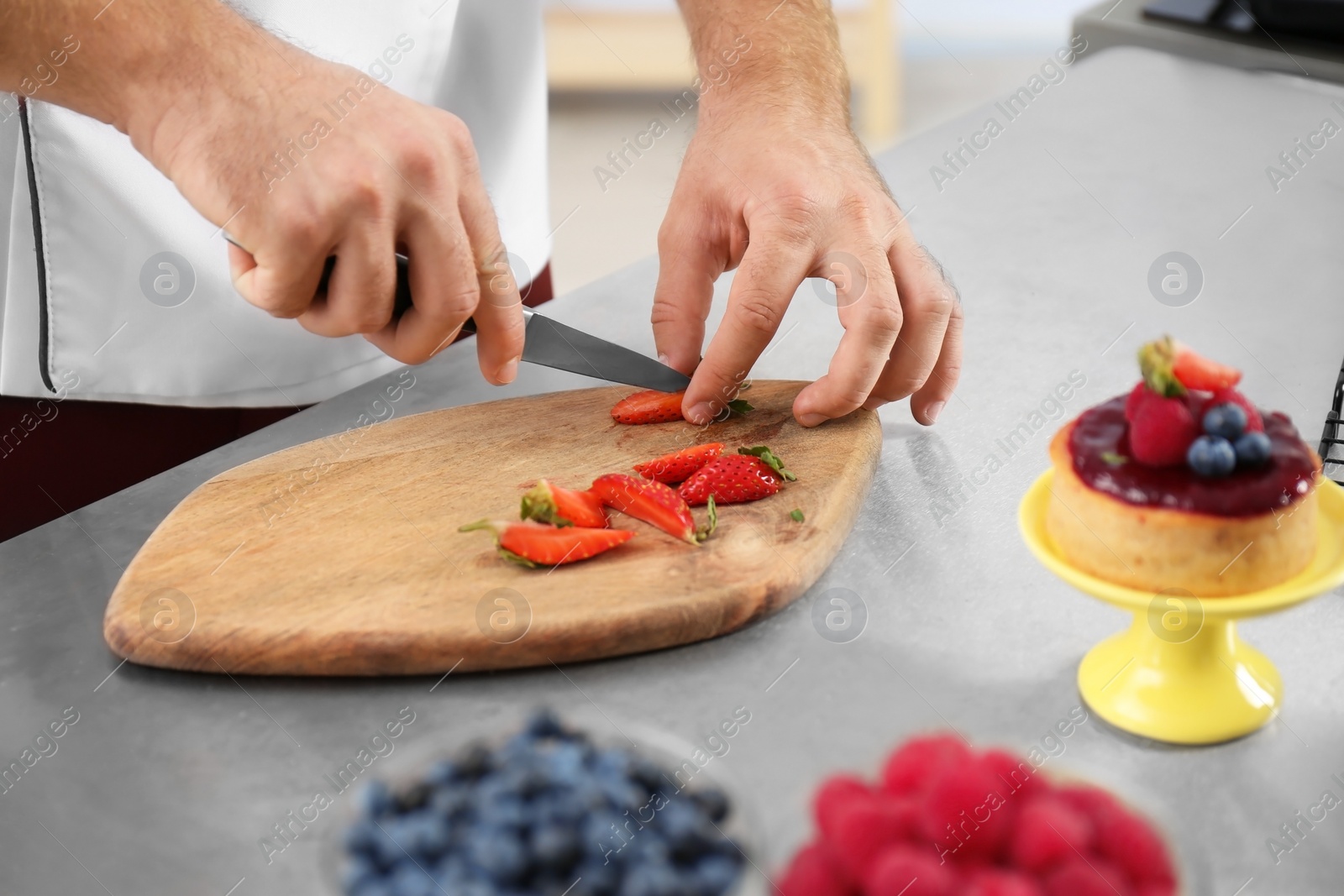 Photo of Male pastry chef cutting berries at table in kitchen, closeup