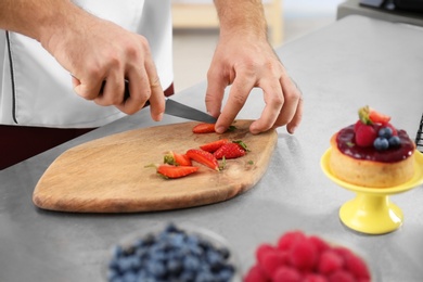 Photo of Male pastry chef cutting berries at table in kitchen, closeup