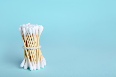 Photo of Bunch of wooden cotton buds on light blue background. Space for text