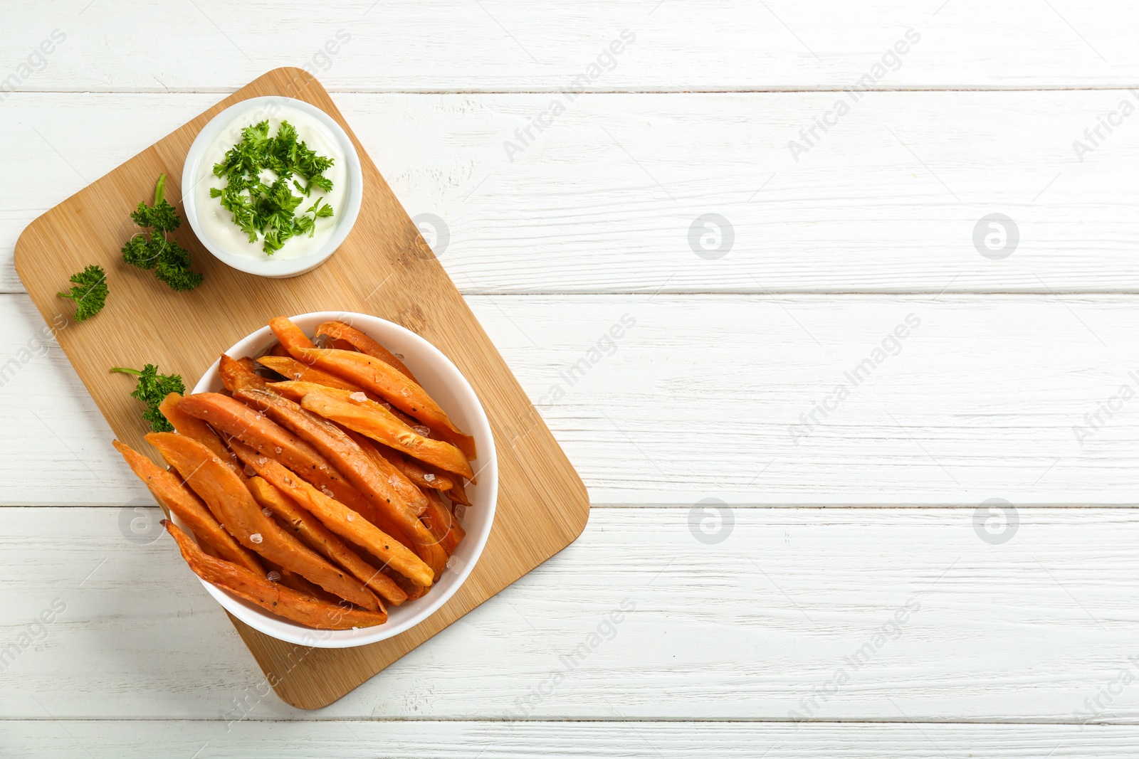 Photo of Bowl with tasty sweet potato fries and sauce on wooden background, top view. Space for text