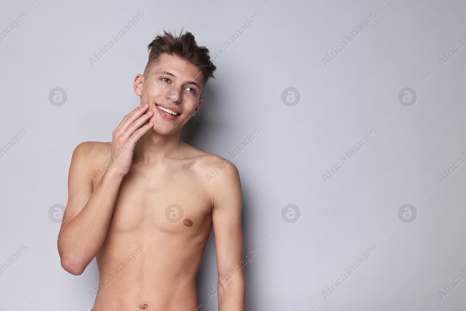 Photo of Handsome man with moisturizing cream on his face against light grey background. Space for text