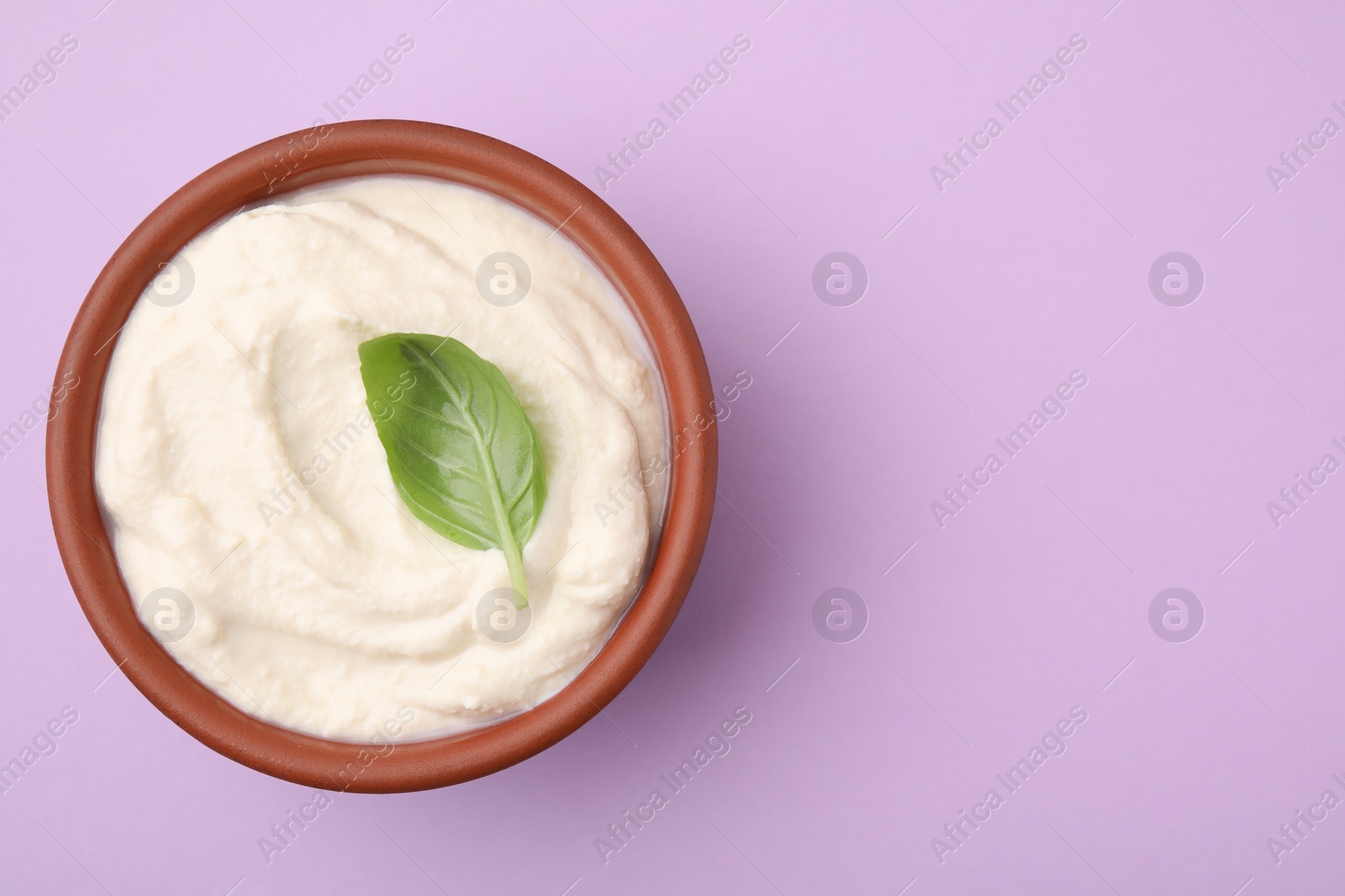 Photo of Delicious tofu sauce and basil leaf in bowl on violet background, top view. Space for text