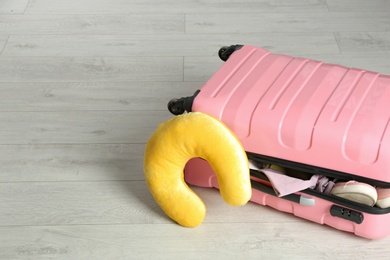 Suitcase with clothes and travel pillow on wooden floor