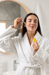 Beautiful young woman applying serum onto her face in bathroom