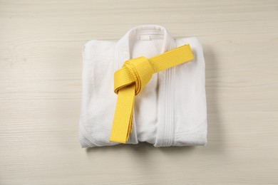 Photo of Yellow karate belt and white kimono on wooden background, top view