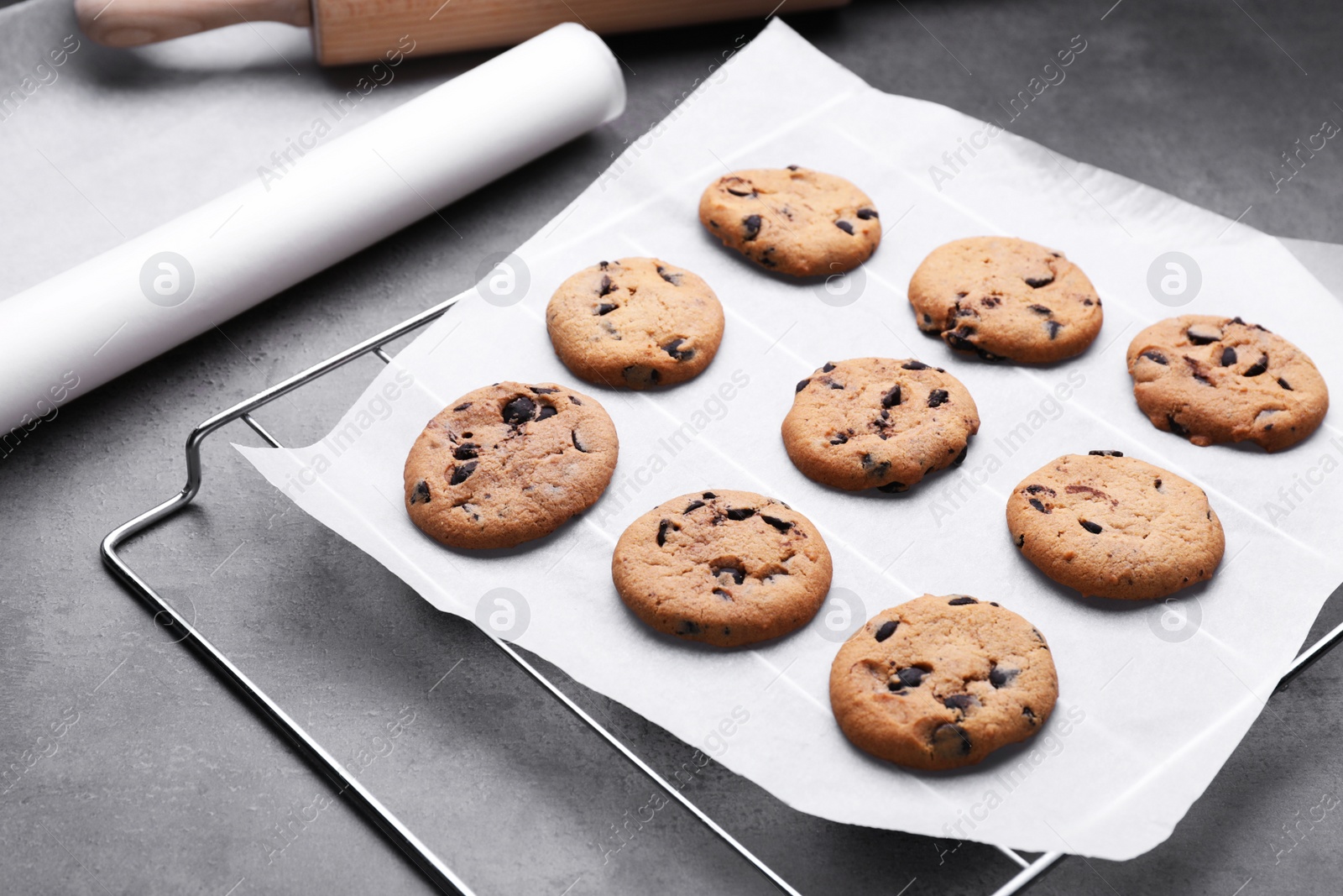 Photo of Roll of parchment baking paper and cooling rack with tasty cookies on dark grey table