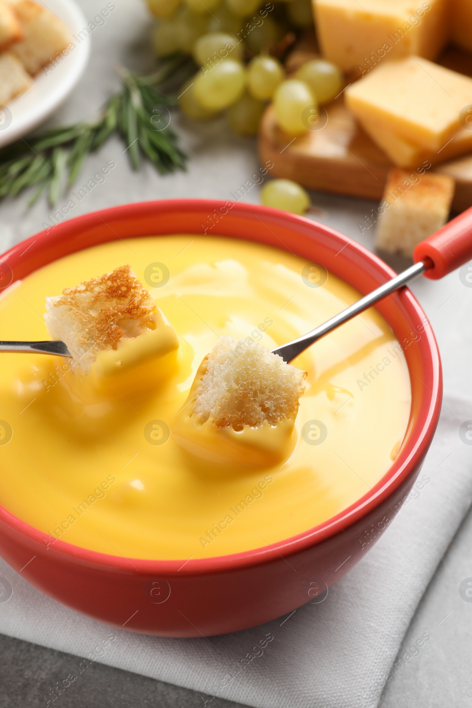 Photo of Pot of tasty cheese fondue and forks with bread pieces at grey table