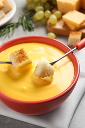 Pot of tasty cheese fondue and forks with bread pieces at grey table