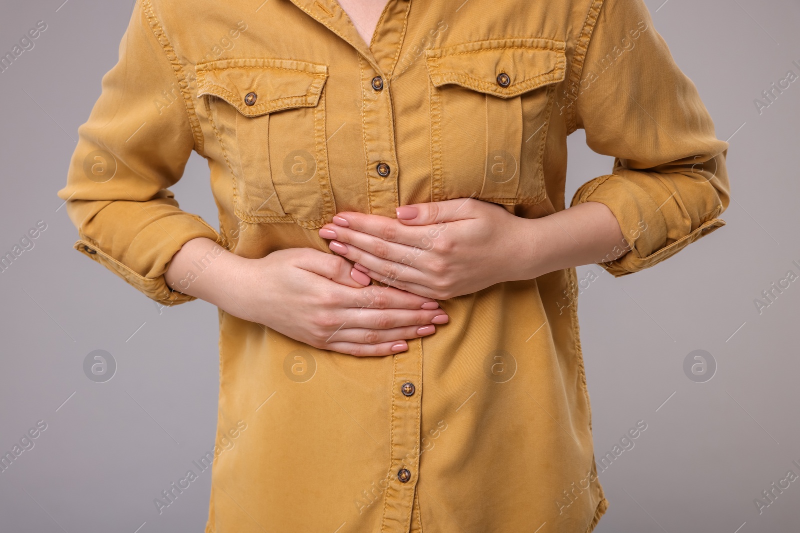 Photo of Young woman suffering from stomach pain on grey background, closeup