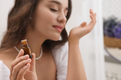 Photo of Beautiful young woman with bottle of essential oil indoors, selective focus