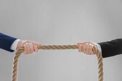 Photo of Dispute concept. Men pulling rope on light grey background, closeup