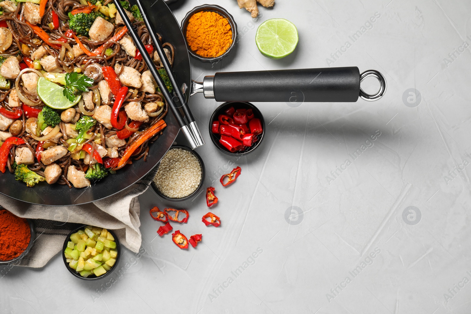 Photo of Stir-fry. Tasty noodles with meat in wok, chopsticks and ingredients on grey textured table, flat lay. Space for text